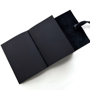 May include: A black leather-bound journal with a black ribbon bookmark. The journal is open to reveal blank pages.
