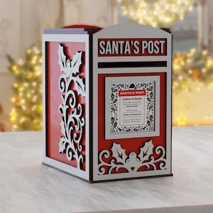 Puede incluir: Un buzón de correo rojo y blanco de Santa's Post de madera con recortes decorativos de acebo y volutas. El buzón tiene un letrero que dice "SANTA'S POST" y un letrero más pequeño con texto. Decoración navideña.