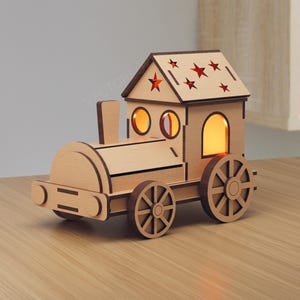 Op de afbeelding: Een houten treinlamp met een huisachtig dak met steruitsparingen. De trein heeft ronde ramen en wielen, en de binnenkant gloeit met warm licht. Het is een decoratief item.