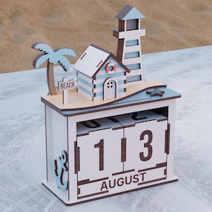 Pode incluir: Um calendário perpétuo de madeira com tema de praia. Apresenta um farol, uma casinha e uma palmeira. A data exibida é "13 AGOSTO". O calendário é pintado em branco, azul e castanho.