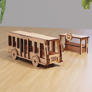 May include: A wooden toy bus and bus stop set. The bus has wheels with cross details and rectangular windows. The bus stop has a sign with a bus icon. Both are made of light brown wood.