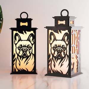 Puede incluir: Dos faroles de madera negra con un diseño de bulldog francés. Los faroles tienen un adorno en forma de hueso y un asa. Uno tiene un lado macizo, el otro un diseño recortado. Los faroles están iluminados con un brillo cálido.