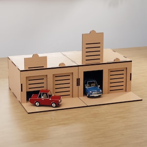 Puede incluir: Un garaje de juguete de madera con tres bahías, cada una con una puerta elevable. Dos coches en miniatura, una camioneta roja y un coche clásico azul, están aparcados dentro. El garaje es de madera clara.