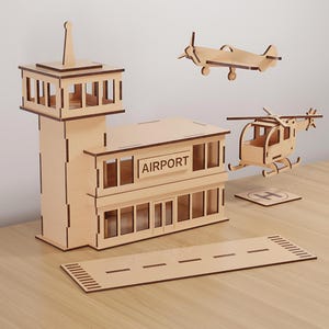 May include: A wooden airport model with a control tower, terminal, runway, airplane, and helicopter. The terminal has the word "AIRPORT" on it. The model is made of light brown wood and is set on a light brown surface.