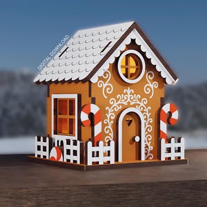 Op de afbeelding: Een peperkoekhuismodel met witte glazuurdetails, zuurstokaccenten en een witte hek. Het huis heeft een bruin dak en staat tegen een vage winterachtergrond. De tekst "DIGITALE DOWNLOAD" is linksboven zichtbaar.