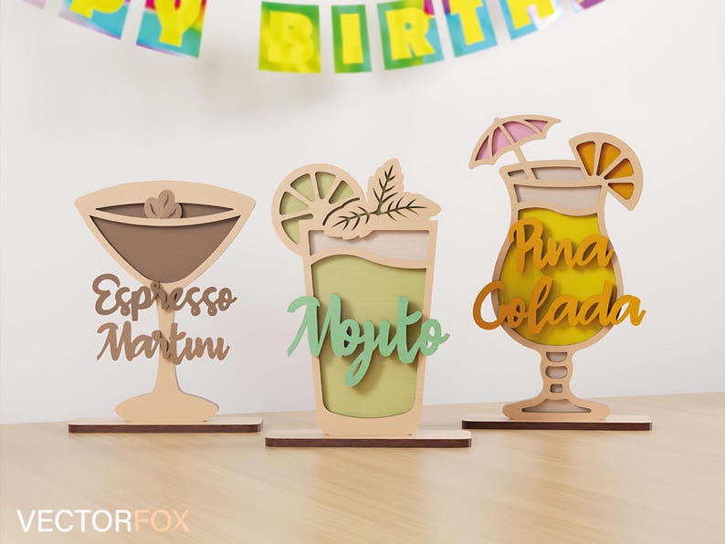 May include: Wooden cocktail decorations, including an espresso martini, mojito, and pi&ntilde;a colada. Each drink is laser-cut with layered details and the drink's name. The decorations are on wooden bases.