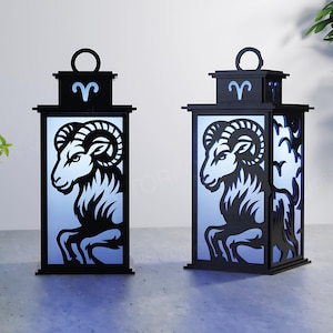 May include: Two black, rectangular lanterns with a ram silhouette design. The lanterns have a handle on top and a light blue background. The ram is a symbol of the Aries zodiac sign. The lanterns are decorative.