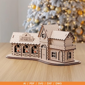 May include: A laser-cut wooden model of a building labelled REINDEER STABLES, featuring three arched stalls with reindeer heads inside, a central tower, and a multi-section roof design. The structure is light tan with dark brown edges.