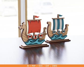 May include: Two wooden Viking ship ornaments mounted on rectangular bases. One ship displays a red sail and a small red flag, whilst the other features a blue and white striped sail with a blue flag. Both ships include blue waves and circular shields.