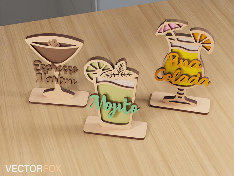 May include: Three wooden cocktail-themed decorations. The first is a martini glass with the text "Espresso Martini". The second is a mojito with the text "Mojito". The third is a pi&ntilde;a colada with the text "Pina Colada".