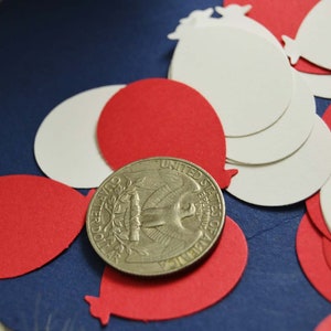 May include: Red and white paper confetti shaped like balloons, scattered on a blue background. A silver US quarter is in the center of the image.