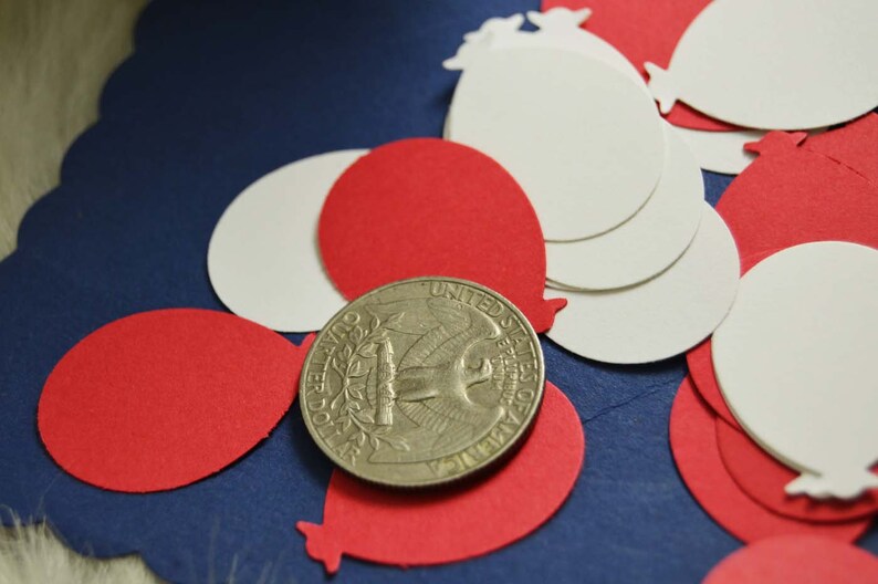 May include: Red and white paper confetti shaped like balloons, scattered on a blue background. A silver US quarter is in the center of the image.