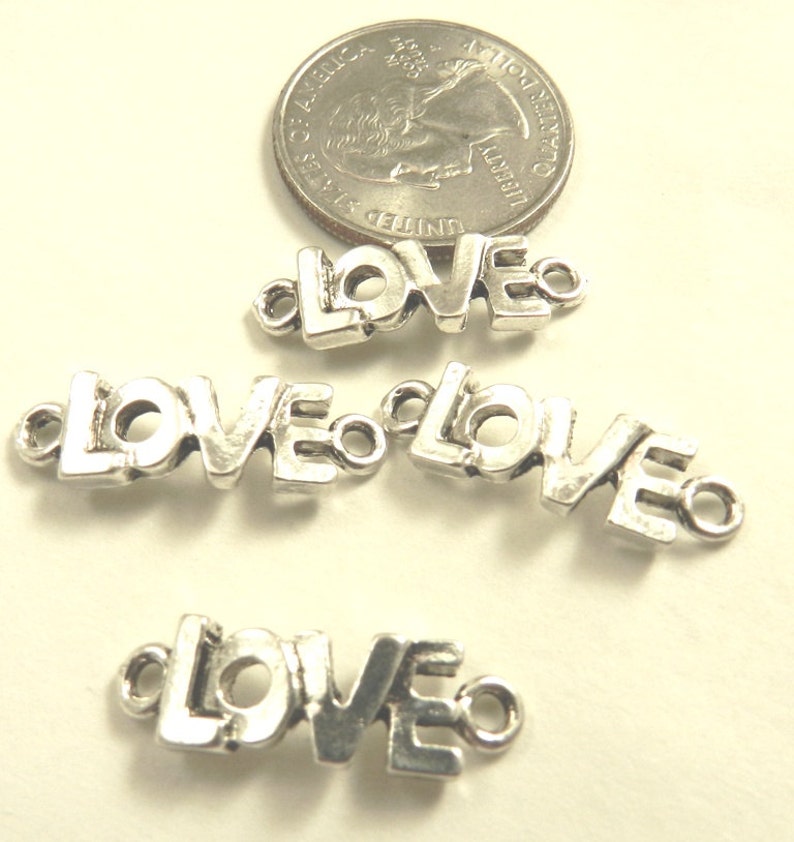 May include: Four silver-toned metal charms in the shape of the word "LOVE". Each charm has two small loops for attaching to a necklace, bracelet, or other jewelry.