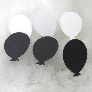 May include: Three pairs of black and white balloon shaped paper cutouts. The balloons are arranged in a row on a white fluffy surface.