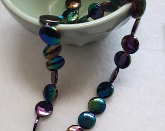 May include: A strand of circular, flat beads featuring an iridescent, metallic finish that shifts between shades of deep purple, blue, and green. The beads are strung together on a thin, light-colored thread, creating a reflective, multi-colored chain.