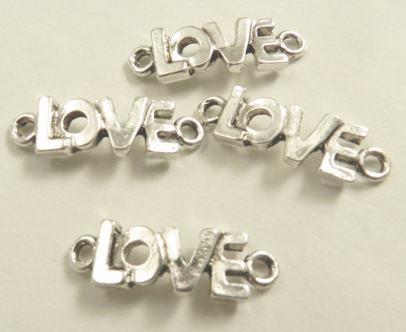 May include: Four silver-toned metal charms, each spelling out the word "LOVE" in a stylized font. The charms have a loop on each end for attaching to jewelry or other crafts.