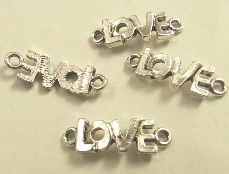 May include: Four silver-toned metal charms, each spelling out the word "LOVE" in a stylized font. The charms have a loop on each end for attaching to jewelry or other crafts.