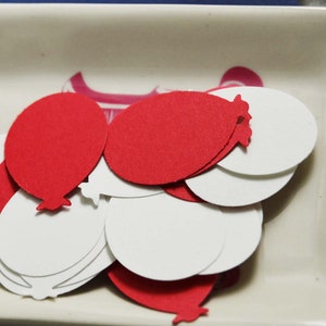 May include: A pile of red and white paper balloon cutouts in a white ceramic dish.