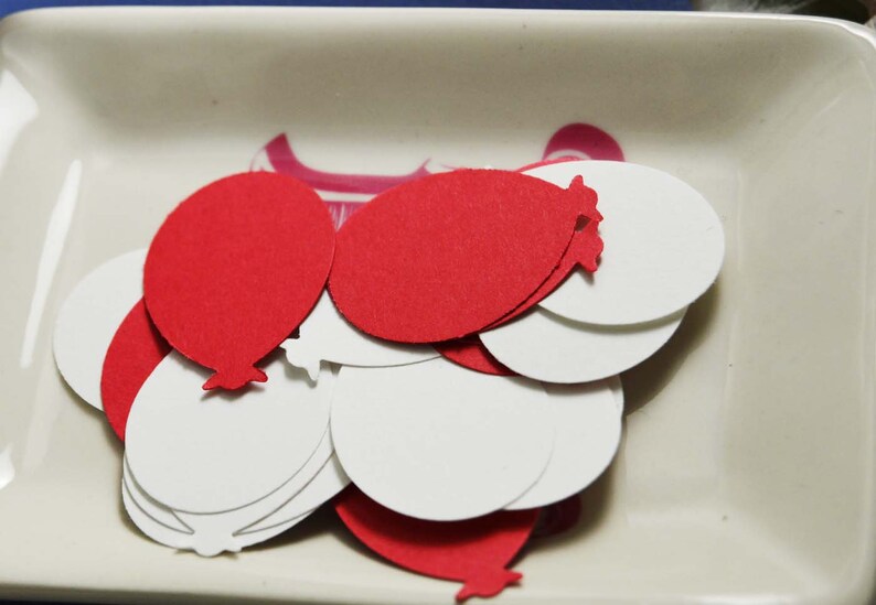 May include: A pile of red and white paper balloon cutouts in a white ceramic dish.