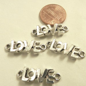 May include: Four silver charm pendants with the word "LOVE" spelled out in a stylized font. Each pendant has a small loop at each end for attaching to a chain or bracelet.