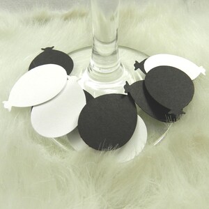 May include: Black and white paper balloon confetti scattered around a wine glass. The confetti is shaped like balloons with a rounded bottom and a pointed top.