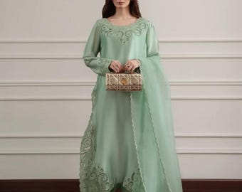 Könnte beinhalten: Ein mintgrünes formelles Outfit. Es besteht aus einer langärmligen Tunika mit gestickten Details, einer passenden Hose und einem transparenten Schal. Eine goldene Clutch wird vor dem Outfit gehalten.