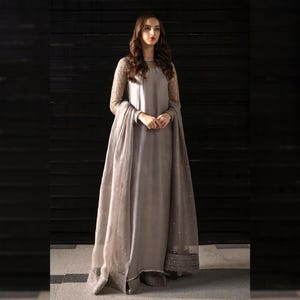 May include: A long, flowing gray dress with sheer, embellished sleeves and a matching shawl. The dress features a high neckline and is adorned with subtle embellishments. The overall design is elegant and suitable for formal occasions.