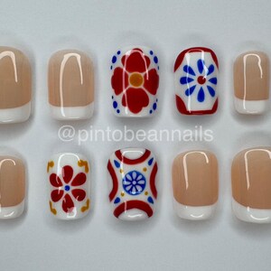 May include: A set of ten press-on nails featuring a mix of classic French manicure designs with nude bases and white tips, alongside accent nails decorated with vibrant red, blue, and yellow floral and geometric patterns. Text reads @pintobeannails.