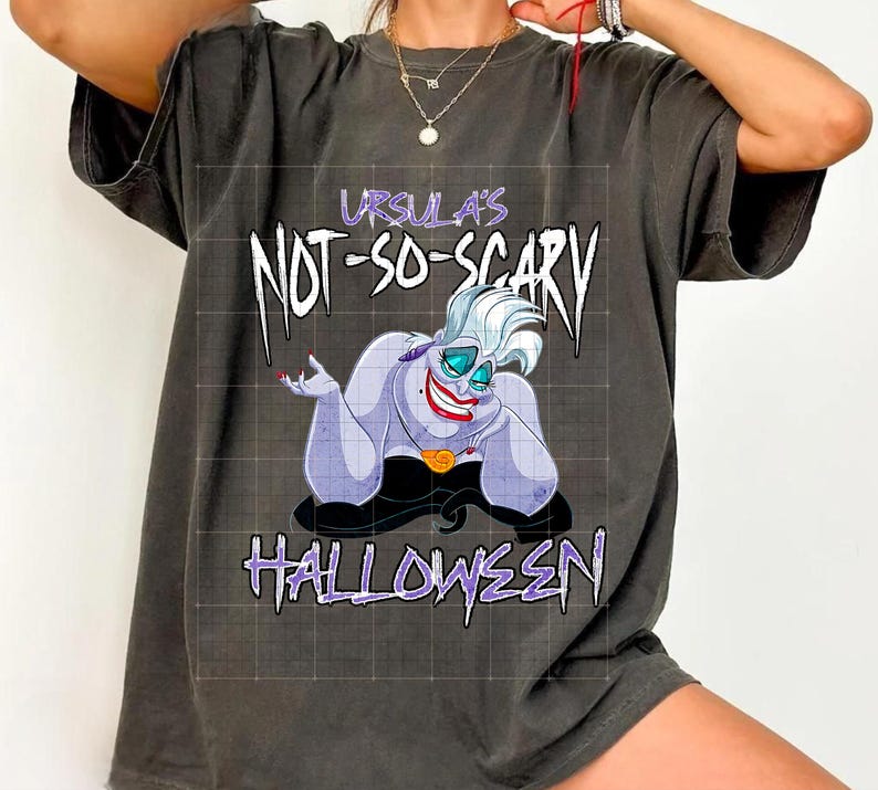 May include: Dark gray t-shirt featuring a cartoon image of Ursula from The Little Mermaid. The text "Ursula's Not-So-Scary Halloween" is printed in white and purple. The shirt is a relaxed fit.