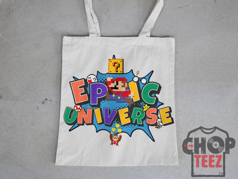 May include: White tote bag featuring a colorful graphic of a pixelated Mario character and the words "EPIC UNIVERSE" in a comic book style. The design includes various game elements and characters.