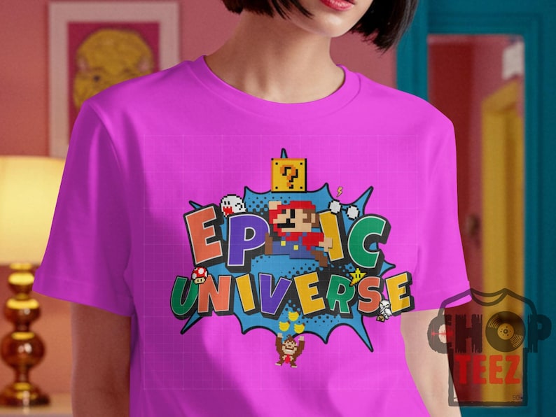 May include: A magenta t-shirt featuring a colorful graphic design. The design includes the words "EPIC UNIVERSE" in a comic book style, along with pixelated characters and elements from a popular video game.