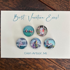 May include: A white card with the teal text "Best Vacation Ever!" and "Glen Arbor, MI." Five circular magnets with vacation photos are attached to the card. The magnets feature family photos.