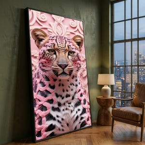 May include: Framed art print featuring a pink leopard with black spots and a detailed face. The leopard is set against a pink, ornate background. The artwork is in a black frame, leaning against a green wall.