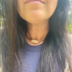 May include: A simple brown cord necklace with a single, off-white, oval-shaped bead.