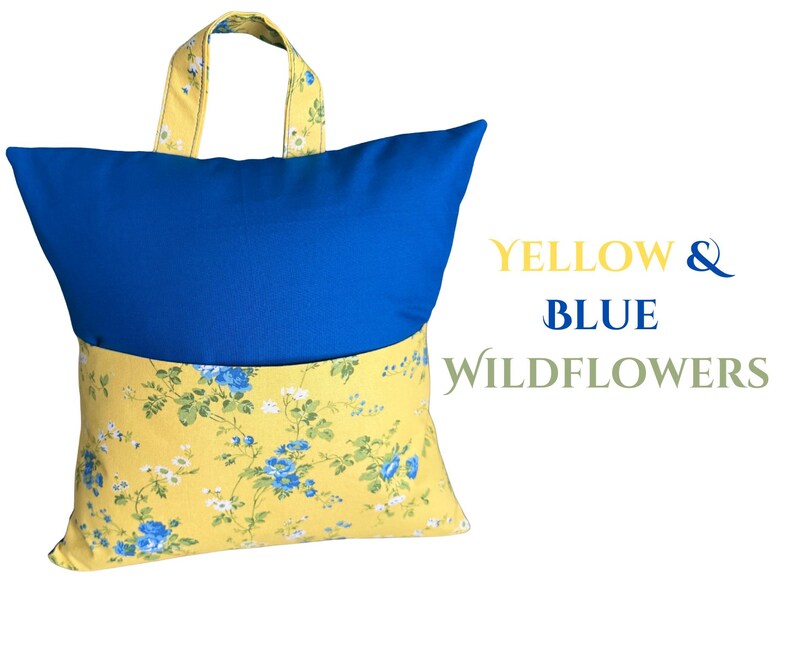 Puede incluir: Una almohada de lectura con la parte superior azul y la inferior floral amarilla. El asa y la parte inferior de la almohada presentan un estampado floral amarillo con flores azules y blancas. El texto "YELLOW & BLUE WILDFLOWERS" est&aacute; a la derecha.