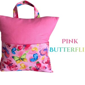 Puede incluir: Una almohada de lectura rosa con asa. La parte superior es rosa liso, mientras que la inferior presenta un estampado de mariposas rosas con mariposas rojas, azules y amarillas. El texto "PINK BUTTERFLIES" se muestra en la imagen.