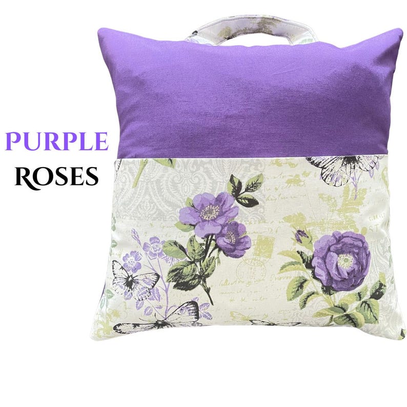 Puede incluir: Un coj&iacute;n decorativo con una parte superior morada y una parte inferior floral. La parte inferior presenta rosas y mariposas moradas sobre un fondo crema. El coj&iacute;n tiene un asa y el texto "PURPLE ROSES".