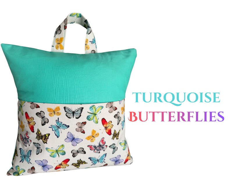 Puede incluir: Una almohada de lectura turquesa y blanca con asa. La parte superior es turquesa lisa, mientras que la inferior presenta una tela blanca estampada con mariposas de colores. El texto "TURQUOISE BUTTERFLIES" es visible a la derecha.