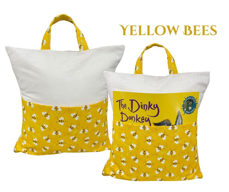 Puede incluir: Dos almohadas para libros blancas y amarillas con asas. La parte inferior de las almohadas y las asas son amarillas con un estampado de abejas. Una almohada tiene un libro en el bolsillo que dice "The Dinky Donkey". El texto "YELLOW BEES" est&aacute; en la parte superior.
