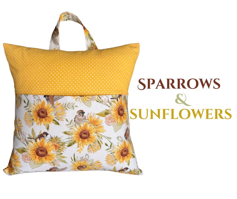 Puede incluir: Una almohada de lectura amarilla con asa. La secci&oacute;n superior es amarilla con lunares blancos. La secci&oacute;n inferior presenta un estampado floral de girasoles y gorriones sobre un fondo blanco. El texto "SPARROWS & SUNFLOWERS" est&aacute; a la derecha.