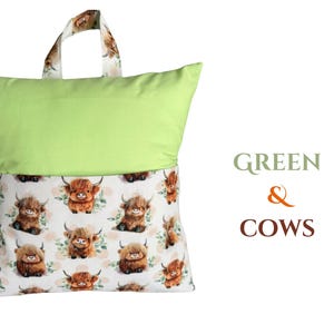 Puede incluir: Una almohada verde con asa, con un estampado de vacas escocesas de dibujos animados sobre un fondo blanco. El asa y la parte inferior de la almohada tienen el estampado de vaca. El texto "GREEN & COWS" est&aacute; a la derecha.