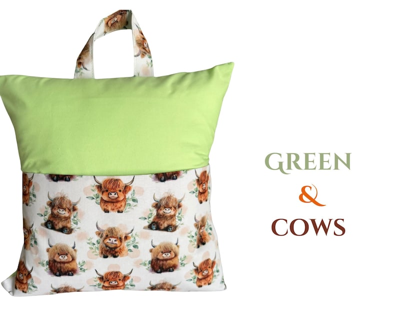 Puede incluir: Una almohada verde con asa, con un estampado de vacas escocesas de dibujos animados sobre un fondo blanco. El asa y la parte inferior de la almohada tienen el estampado de vaca. El texto "GREEN & COWS" est&aacute; a la derecha.