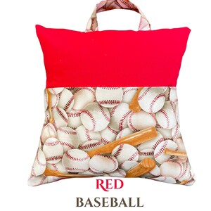 Puede incluir: Una almohada de lectura roja con asa. La secci&oacute;n superior es de color rojo liso, mientras que la inferior presenta un estampado de pelotas de b&eacute;isbol blancas y bates de madera. El texto "RED BASEBALL" est&aacute; impreso en la parte inferior.