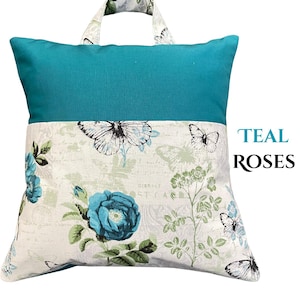 Puede incluir: Coj&iacute;n de lectura turquesa y blanco con asa. La parte superior es turquesa y la inferior presenta un estampado floral y de mariposas. El texto "TEAL ROSES" est&aacute; en el lado derecho del coj&iacute;n.