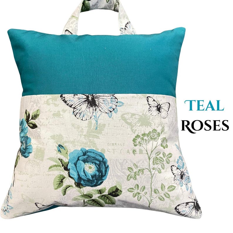 Puede incluir: Coj&iacute;n de lectura turquesa y blanco con asa. La parte superior es turquesa y la inferior presenta un estampado floral y de mariposas. El texto "TEAL ROSES" est&aacute; en el lado derecho del coj&iacute;n.