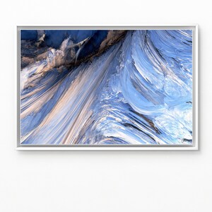 May include: Abstract art print in a silver frame. The artwork features a dynamic composition of swirling blue, white, and tan colors, creating a sense of movement and depth. The piece evokes a feeling of flowing water or wind.
