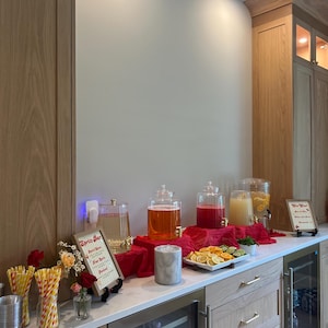 May include: A beverage station with clear glass drink dispensers filled with various colorful drinks. A sign that says "Sprite Bar" is displayed. The station includes a selection of sliced citrus fruits and decorative elements.