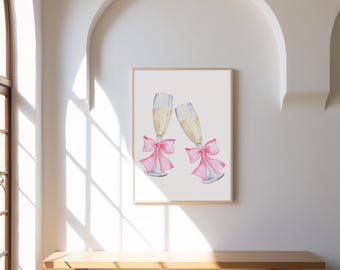 May include: A framed watercolour print featuring two champagne flutes, each with a pink bow. The flutes are filled with a golden liquid. The artwork is displayed on a white wall above a wooden bench. The frame is made of wood.