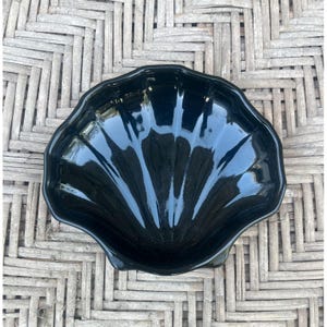 Könnte beinhalten: Eine glänzend schwarze, muschelförmige Schale. Die Schale hat einen gewellten Rand und eine glatte, reflektierende Oberfläche. Die Schale ist wahrscheinlich aus Glas oder Keramik und eignet sich zum Servieren von Speisen oder als Dekorationsartikel.
