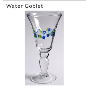 Könnte beinhalten: Klares Wasserglas mit ausgestellter Oberseite und einem dekorativen Band aus blauen und grünen quadratischen Akzenten. Das Glas hat einen abgerundeten Stiel und einen kreisförmigen Fuß. Der Text "Water Goblet" steht oben.